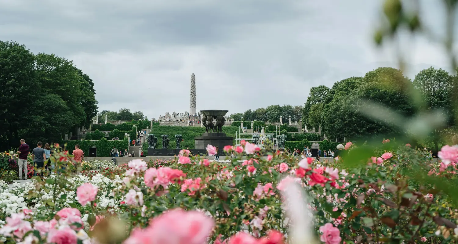 Vigeland Park in summer, with the rose garden in front of the Fountain and the Monolith Caption: The full axis in one frame — roses, the Fountain, and the Monolith on the plateau behind.
